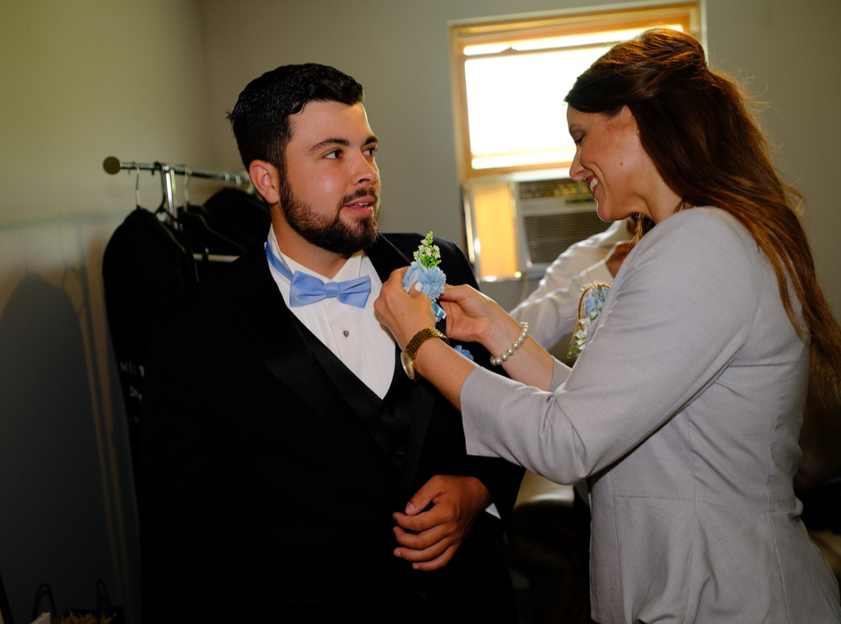 wedding coordinator pinning blue boutonniere onto groom