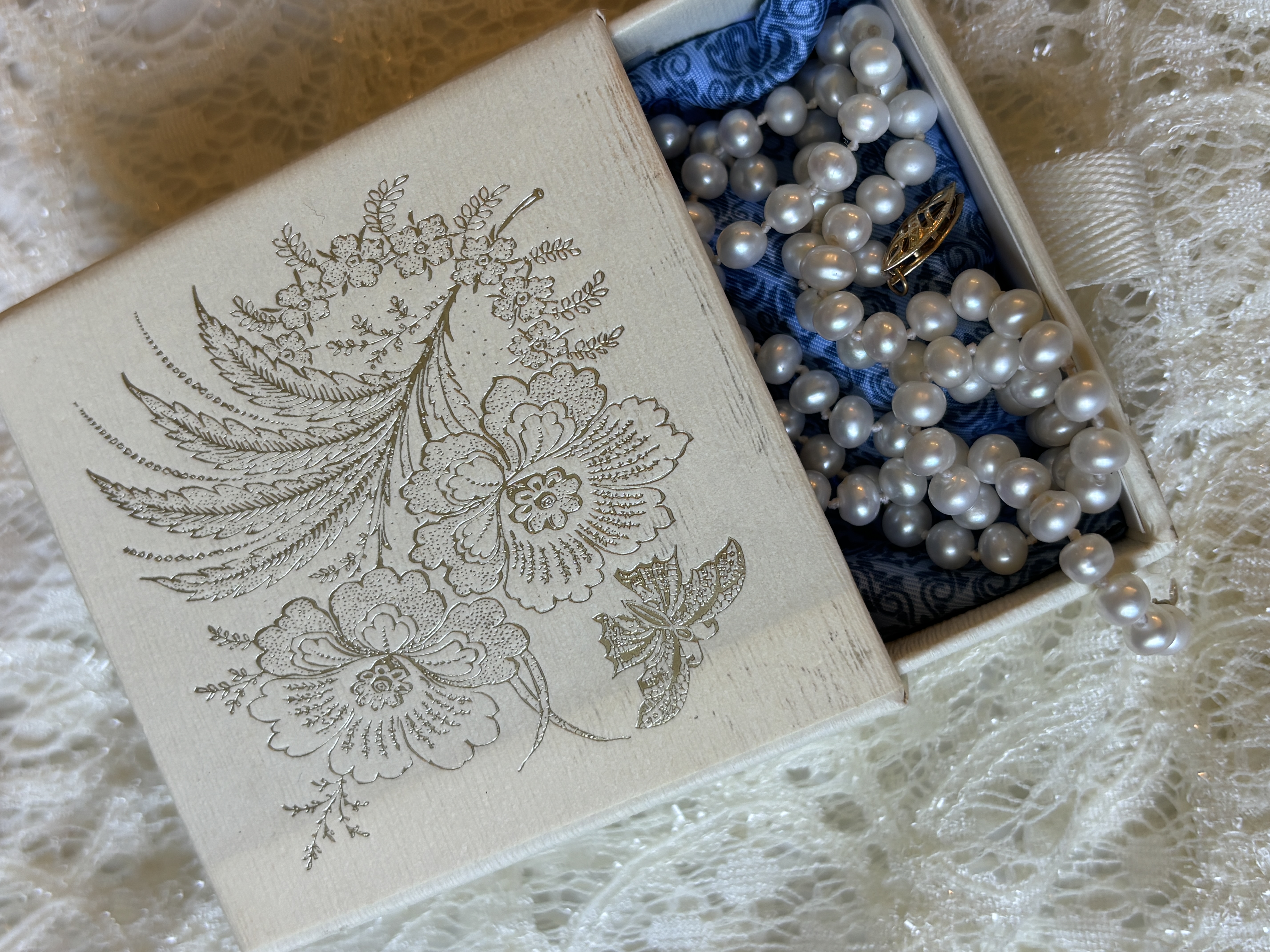 embossed ivory box partially open to reveal blue lining and pearls
